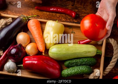 Una donna irriconoscibile sta tenendo un pomodoro su uno sfondo di verdure diverse. Il concetto di cibo sano, vegetarianismo. Foto Stock