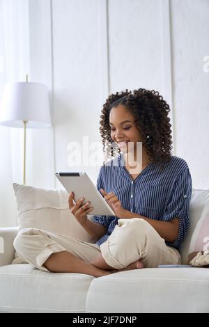 Felice misto ha corso ragazza africana adolescente seduto sul divano tenendo con tablet. Foto Stock