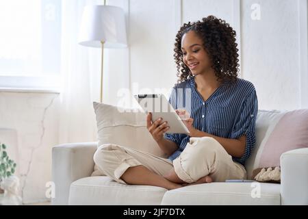 Felice ragazza africana teen utilizzando la tecnologia tablet digitale seduto sul divano a casa. Foto Stock