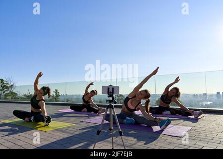 Diverse donne gruppo di tiro online lezione di stretching tutorial all'aperto sul telefono. Foto Stock