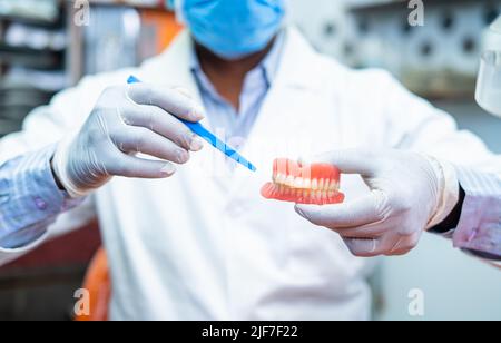 Primo piano di Dentist mani in clinica consigliare o dire circa la cavità dei problemi dei denti tenendo la dentiera mentre si guarda la macchina fotografica - concetto di Foto Stock