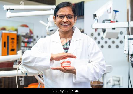 Buon dentista sorridente che tiene le dentature nelle mani guardando la macchina fotografica all'ospedale - concetto di occupazione professionale, di trattamento e di cura orale Foto Stock