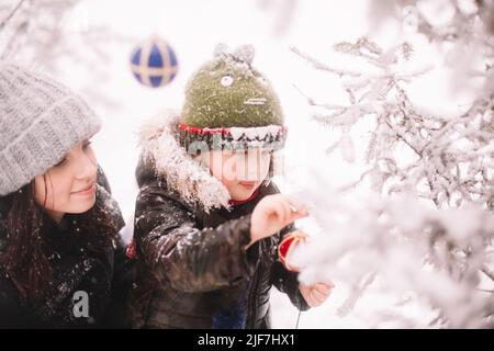 Bambino e sua madre decorano l'albero di natale all'aperto in inverno Foto Stock