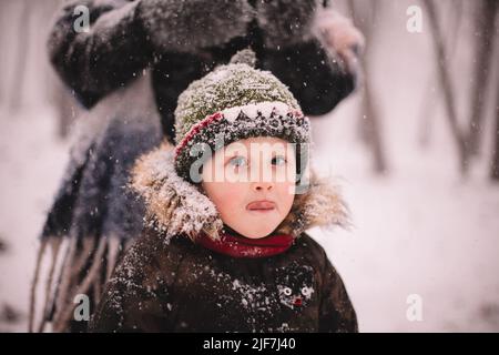 Ritratto del bambino carino in piedi all'aperto durante la nevicata in inverno Foto Stock