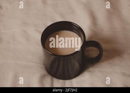 coppa nera con latte cremoso a letto Foto Stock