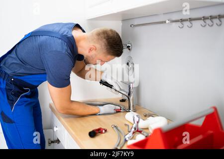 Felice Giovane Maschio Plumber che fissa il rubinetto in cucina Foto Stock