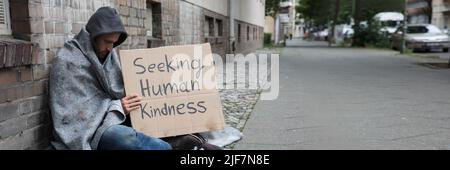 Mendicante maschio nel cofano mostra cerca di gentilezza umana segno su cartone Foto Stock