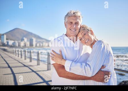 Una coppia caucasica matura felice godendo aria fresca in vacanza in spiaggia. Sorridente coppia in pensione abbracciando e abbracciando mentre si unisce all'esterno Foto Stock