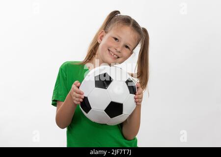 Una ragazza carina in una t-shirt verde con una palla di calcio in mano sorride isolato su uno sfondo bianco. Un bambino caucasico sportivo tiene la palla. Bambini Foto Stock