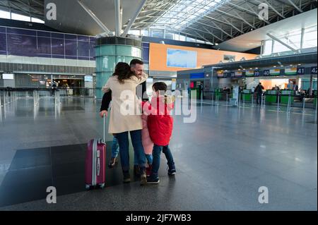 Felice giovane famiglia che abbraccia all'aeroporto. Il marito abbraccia sua moglie e i suoi figli dopo il ritorno da un viaggio d'affari nel terminal degli arrivi dell'hotel Foto Stock