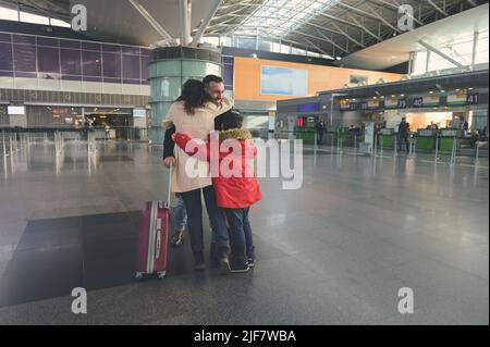 Felice amorevole donna e suo figlio incontrare suo marito, papà dopo un viaggio d'affari nel terminal degli arrivi dell'aeroporto internazionale. I membri della famiglia abbracciano, Foto Stock