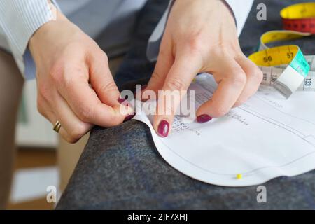 Giovane sneamstress che si aggraffa il modello di carta sul tessuto. Donna su misura sews vestiti con le proprie mani Foto Stock