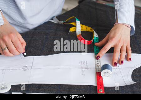 Il dressmaker contrassegna un pezzo di tessuto con gesso in base al modello di carta. Lavoro di sarto, utensili per cucire Foto Stock