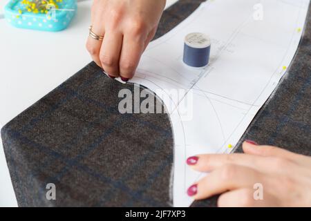 Il dressmaker contrassegna un pezzo di tessuto con gesso in base al modello di carta. Lavoro di sarto, utensili per cucire Foto Stock