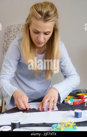 Giovane sneamstress che si aggraffa il modello di carta sul tessuto. Donna su misura sews vestiti con le proprie mani Foto Stock