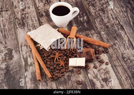 tazza di caffè con cioccolato, bastoncini di cannella e chicchi di caffè su sfondo di legno Foto Stock