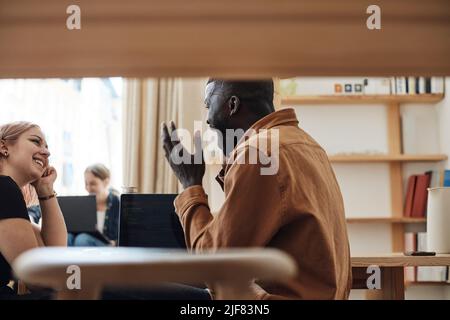 Vista laterale di un uomo d'affari che ride mentre guarda una collega in ufficio Foto Stock