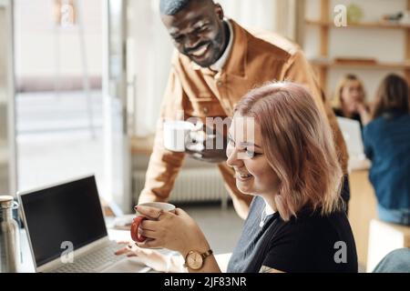 Vista laterale dell'imprenditore sorridente che tiene la tazza di caffè vicino con il collega in ufficio Foto Stock