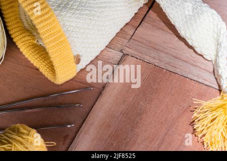 cappellino di elfo del bambino uncinetto, messo su assi di legno, due rotoli di filato giallo e bianco accanto ad esso, materiali per iniziare uncinetto. concetto di lavoro Foto Stock