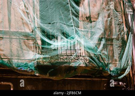 Rete di protezione. Ricostruzione della facciata di un classico edificio storico di appartamenti sulla strada della città. Facciata verde rete di costruzione copre una vecchia casa b Foto Stock