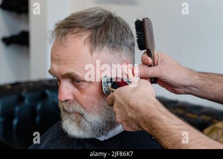 Un uomo anziano che intruda i capelli di un maestro in un barbiere. Un vecchio uomo ottiene un taglio di capelli elegante Foto Stock