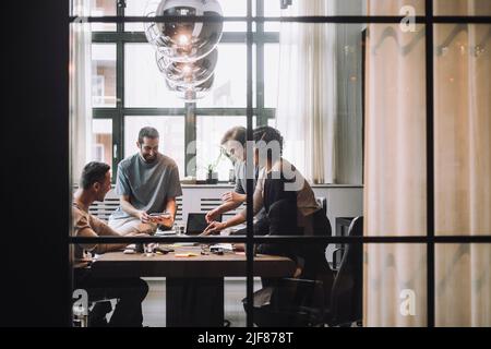 Sorridenti uomini d'affari e donne d'affari che discutono nella sala riunioni vista attraverso il vetro Foto Stock