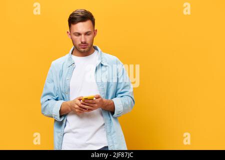 Triste frustrato giovane pensivo abbronzato bell'uomo in blu base t-shirt tenere telefono guardare da parte posa isolato su sfondo giallo studio. Spazio di copia Foto Stock