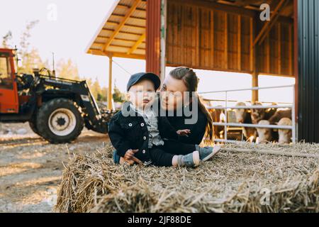 Madre che guarda il figlio seduto sul fieno balla in fattoria Foto Stock