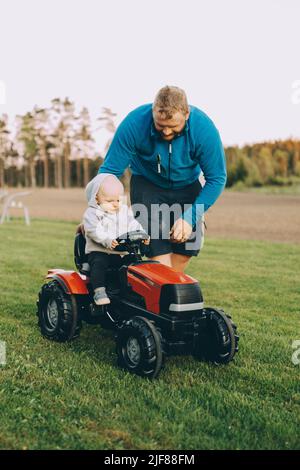 Padre che dà il giro al figlio seduto in trattore giocattolo in fattoria Foto Stock