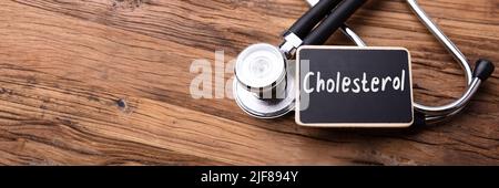Colesterolo parola scritta su ardesia con uno stetoscopio sul tavolo di legno Foto Stock
