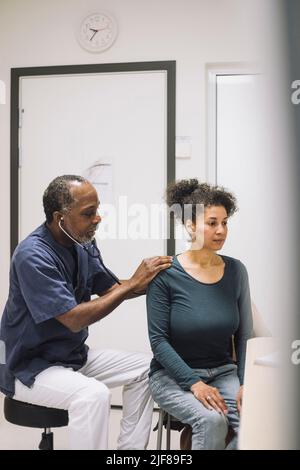 Medico di sesso maschile che esamina la paziente con stetoscopio in clinica medica Foto Stock