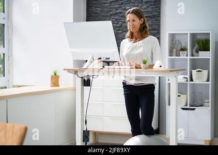 Donna che usa la scrivania regolabile in altezza in ufficio per una buona postura Foto Stock