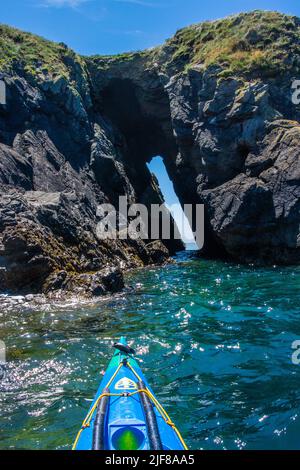 Kayak in mare attraverso un arco di roccia al largo della costa di Pembrokeshire in Galles Foto Stock