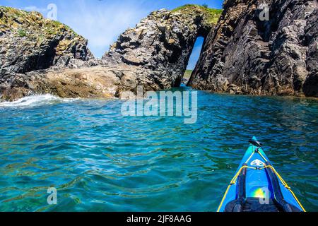 Kayak in mare attraverso un arco di roccia al largo della costa di Pembrokeshire in Galles Foto Stock