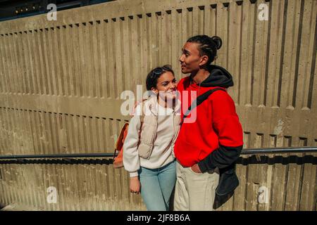 Giovane donna sorridente in piedi con un amico maschio contro il muro il giorno di sole Foto Stock