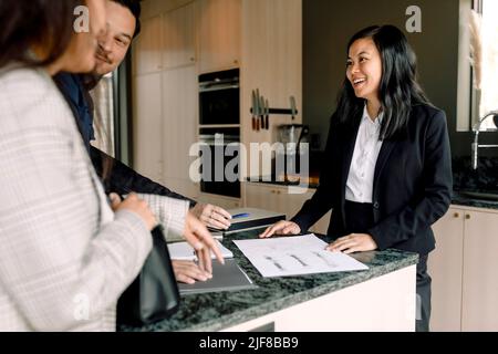 Un realtor sorridente che spiega ai clienti i documenti della nuova casa Foto Stock