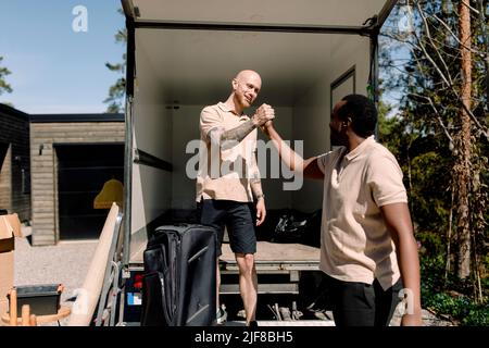 I dipendenti dell'azienda di consegna multirazziale scuotono le mani mentre si trovano all'esterno del veicolo Foto Stock