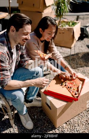 Sorridente coppia mangiare pizza mentre si ricollocano in casa nuova Foto Stock