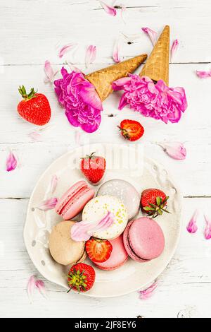 Macaron con fragole e peonie fiori petali, su sfondo bianco di legno. Dolce dessert, stile romantico, piatto, luce dura, ombra scura, Foto Stock