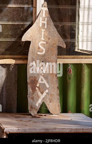 Vecchio segno di freccia di legno che dice 'questo senso' propped contro il muro di una capanna abbandonata dei minatori dello zaffiro a Rubyvale Australia Foto Stock