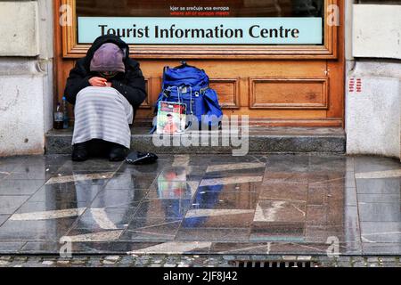 Un uomo senza tetto ripara dalla pioggia al di fuori del centro di informazioni turistiche a Lubiana, capitale della Slovenia. Foto Stock