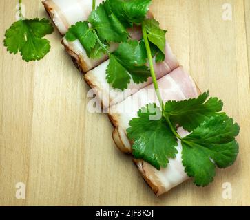 Taglio curvo piegato in rotoli. Maiale su un tavolo da cucina con prezzemolo. Ancora vita di carne. Antipasto di maiale alla pancia. Foto Stock