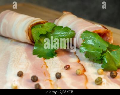 Taglio curvo piegato in rotoli. Maiale su un tavolo da cucina con prezzemolo. Ancora vita di carne. Antipasto di pancia di maiale. Pancetta con prezzemolo Foto Stock