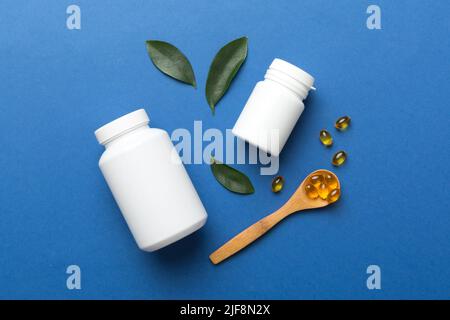 Le capsule di Omega-3 si trovano in un flacone bianco su un tavolo con il fondo verde delle foglie. Compresse di olio di pesce. Additivi biologicamente attivi omega 6, omega 9, vitam Foto Stock