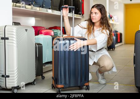 Cliente positivo e allegro che sceglie la valigia da viaggio in negozio Foto Stock