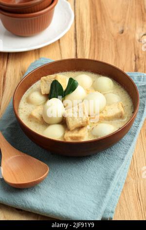 Opor Tahu Telur Puyuh o curry indonesiano con tofu e uovo di quaglia, servito su ciotola di ceramica, su tavola di legno Foto Stock