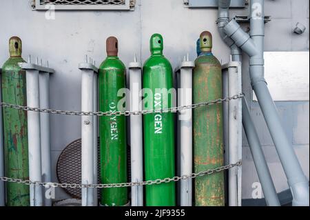 Le bombole di gas compresso vengono immagazzinate verticalmente fissate da una catena metallica e da un tappo metallico. Foto Stock