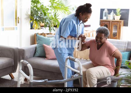 Giovane medico afroamericano che aiuta le donne anziane a alzarsi dal divano a casa Foto Stock