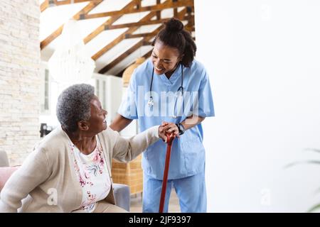 Medico afroamericano che aiuta la donna anziana ad alzarsi dal divano a casa, spazio copia Foto Stock