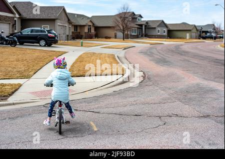 Ragazza che guida una bicicletta in modo sicuro attraverso la strada fino a un marciapiede indossando un casco. Foto Stock